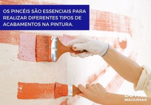Duas mãos segurando pincéis de tamanhos diferentes, pintando parede branca com tinta laranja,.