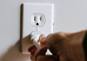 mão colocando um plug em uma tomada branca na parede branca