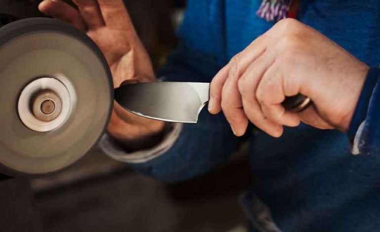 Homem afiando faca em roda de afiar